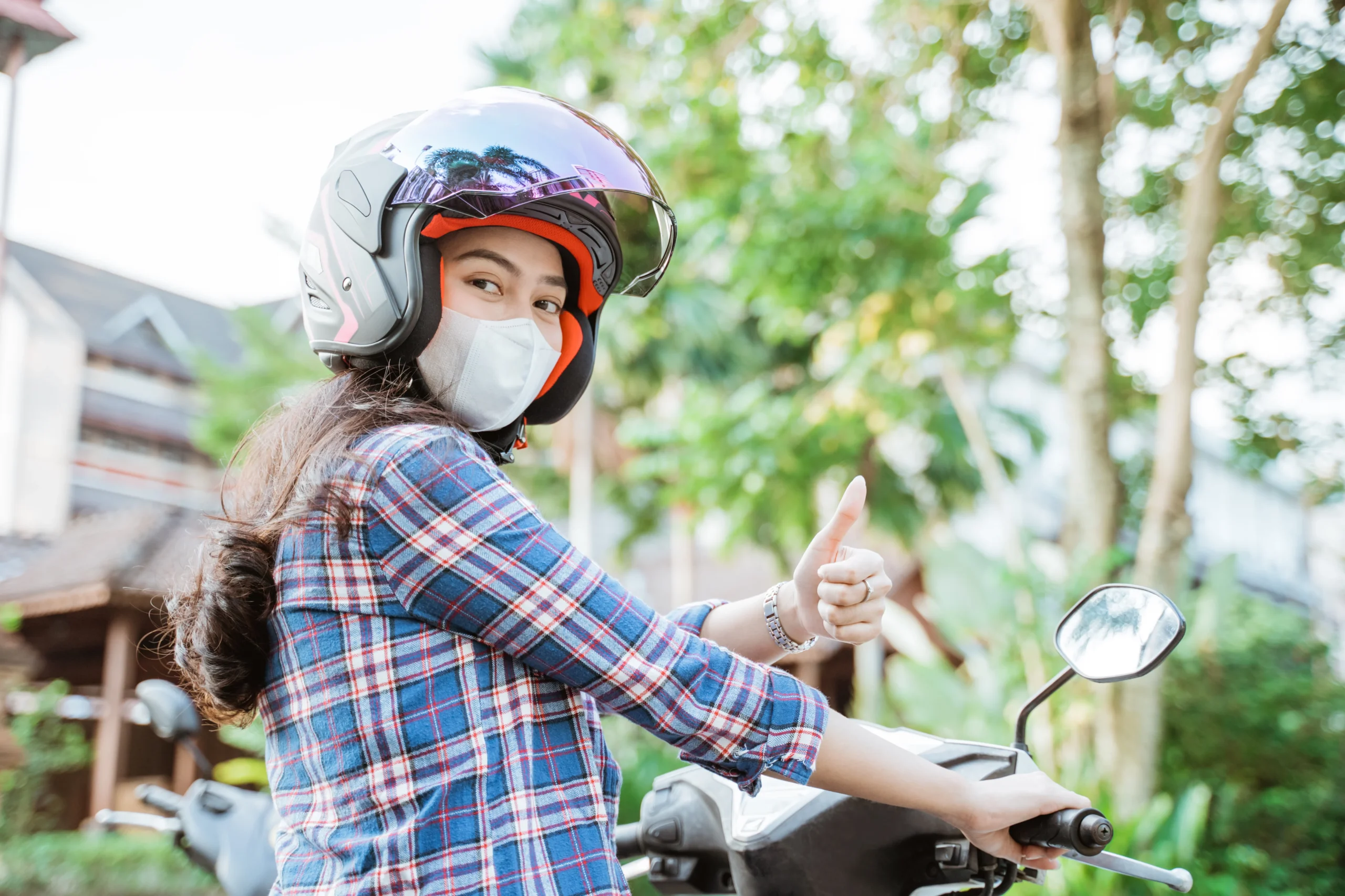 woman wearing helmet and mask with thumbs up while riding
